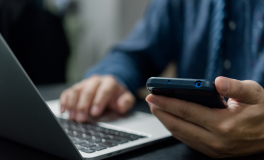 A person holding a phone looks up a contact number on a laptop.